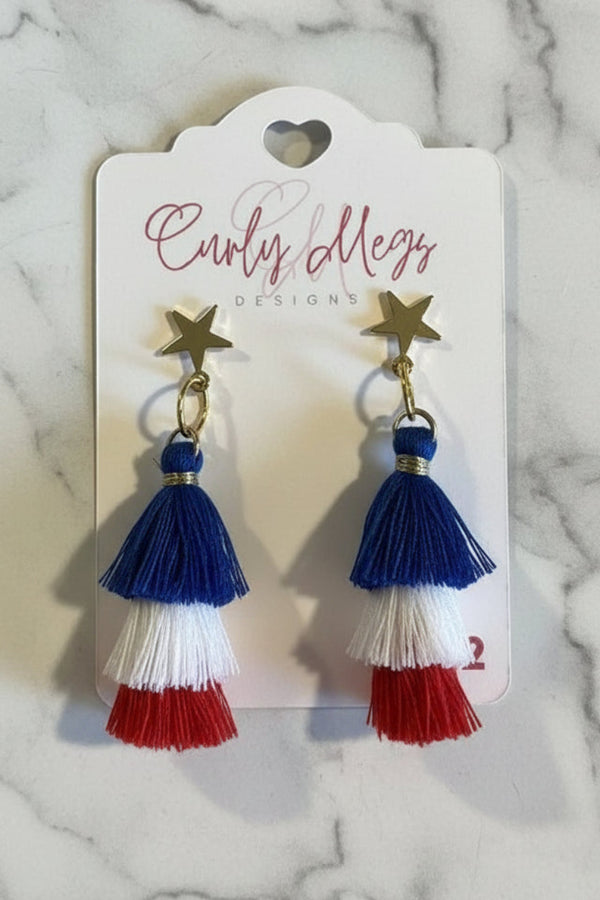 Curly Megs Designs tiered tassel earrings in red, white, and blue with gold star accents.